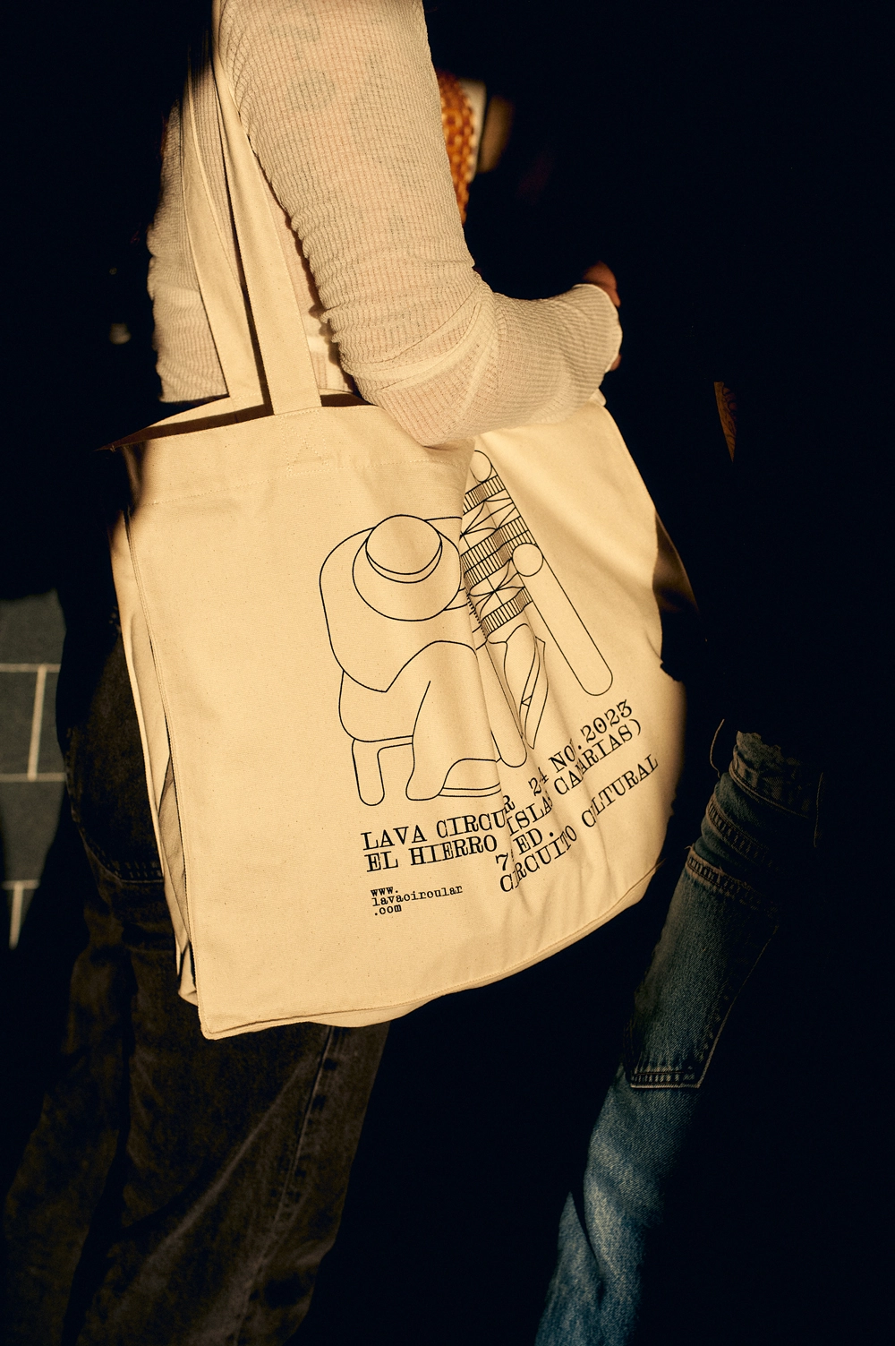 A close-up of a tote bag from the Lava Circular event featuring an illustration by Jhon Boy of a figure playing a drum. The bag prominently displays event details: “Lava Circular, El Hierro, 2–4 Nov 2023, 7a edición, Circuito Cultural.” The design captures the event’s artistic and cultural spirit. Photograph by Adrian Rios.